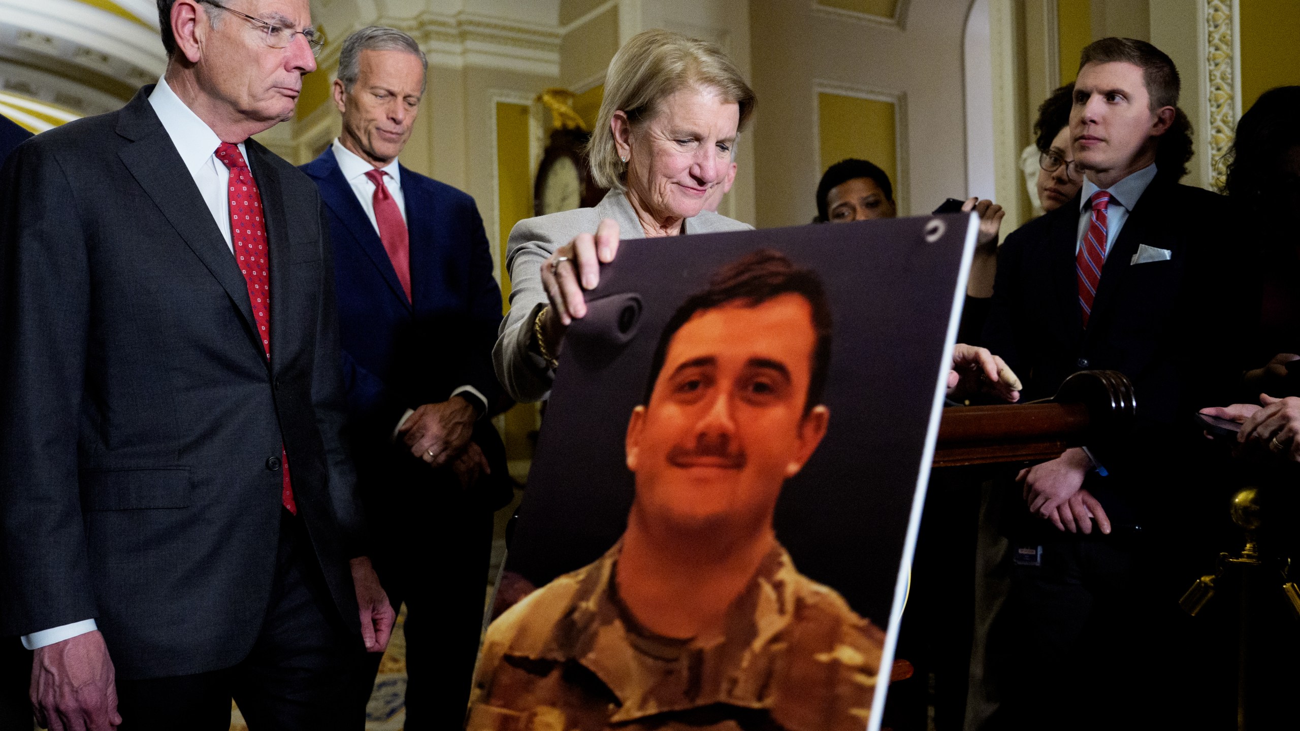 Sen. Shelley Moore Capito (R-WV), accompanied by Senate Majority Whip John Barrasso (R-WY) (L), and Senate Majority Leader John Thune (R-SD) (2nd-L), holds an image of West Virginia Army National Guard Staff Sgt. Andrew Wolfe, 24.