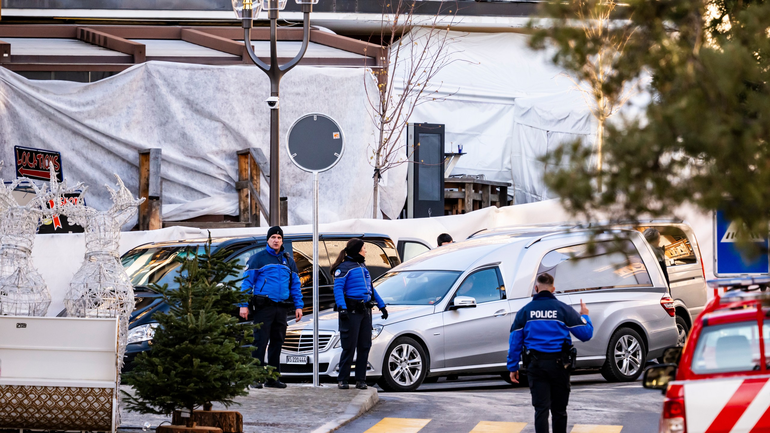A hearse drives past as police officers inspect the area where a fire broke out at the Le Constellation bar and lounge during New Year's celebration, in Crans-Montana, Switzerland, Thursday, Jan. 1, 2026. (Jean-Christophe Bott/Keystone via AP)