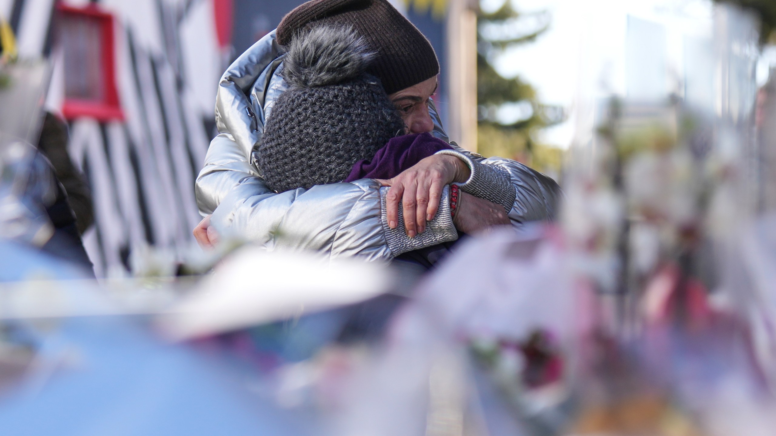 People mourn behind flowers and letters near the sealed off Le Constellation bar, where a devastating fire left dead and injured during the New Year's celebrations in Crans-Montana, Swiss Alps, Switzerland, Friday, Jan. 2, 2026. (AP Photo/ Antonio Calanni)