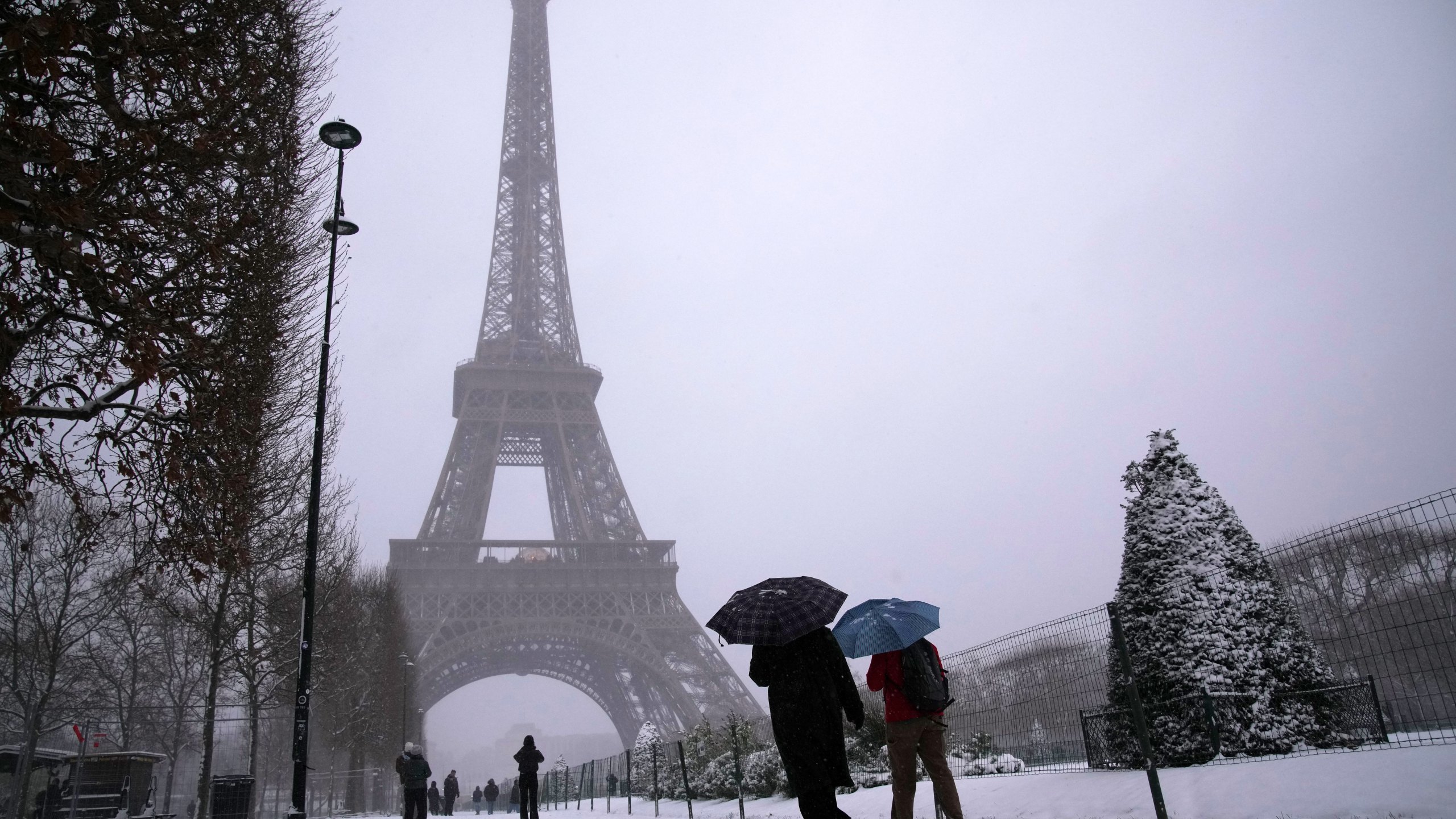 People walk near the Eiffel Tower during a snowfall Wednesday, Jan. 7, 2026 in Paris. (AP Photo/Christophe Ena)
