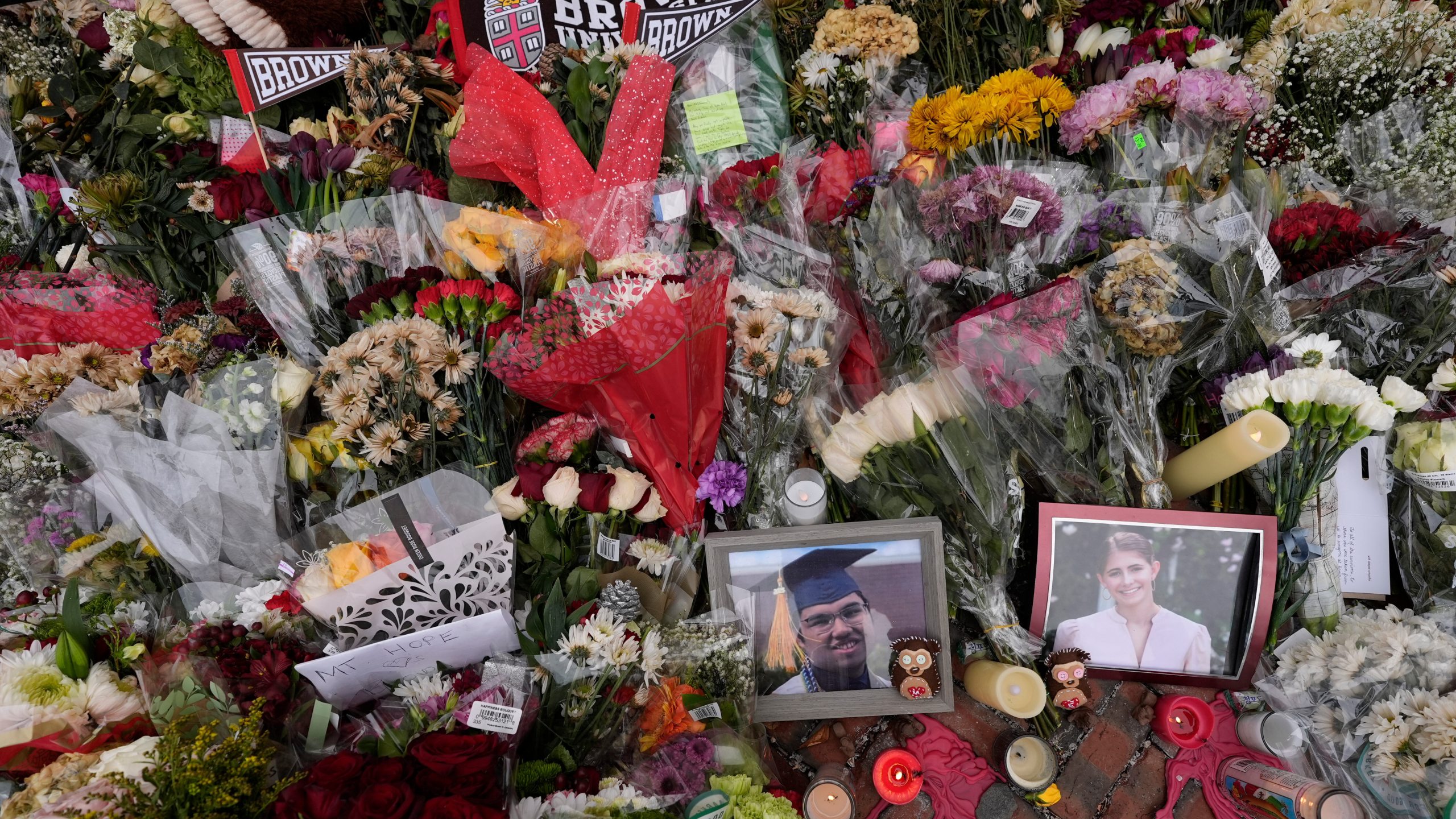 FILE - Photos of Brown University shooting victims Mukhammad Aziz Umurzokov, left, and Ella Cook, are seen amongst flowers at a makeshift memorial at the school's Van Wickle Gate, Dec. 17, 2025, in Providence, R.I. (AP Photo/Robert F. Bukaty, File)