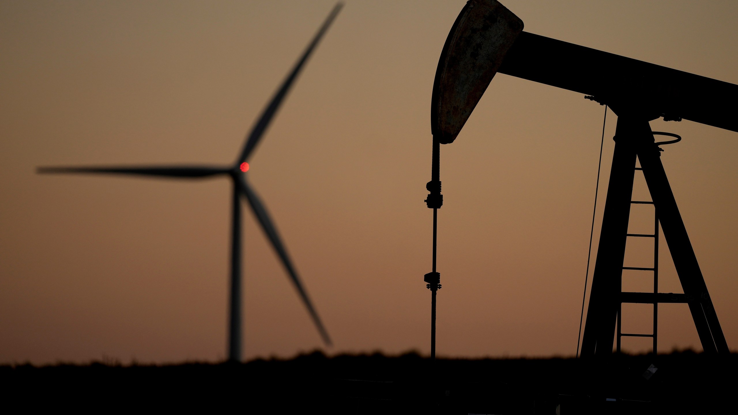FILE - A pumpjack operates in the foreground while a wind turbine at the Buckeye Wind Energy wind farm rises in the distance, Sept. 30, 2024, near Hays, Kan. (AP Photo/Charlie Riedel, File)