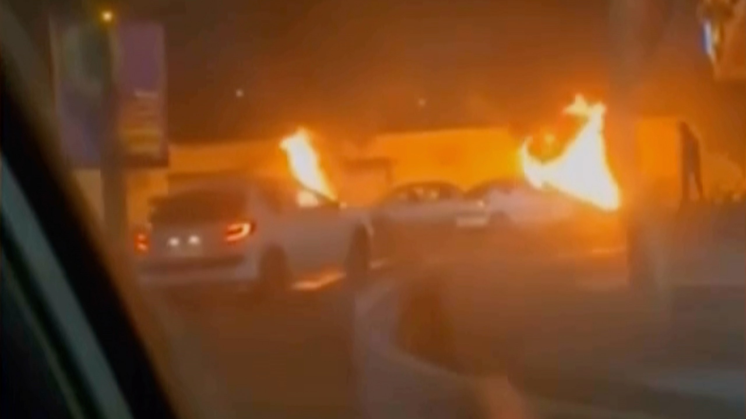 This frame grab from a video released Friday, Jan. 9, 2026, by Iranian state television shows cars driving past burning vehicles during a night of mass protests in Tehran, Iran. (Iranian state TV via AP)