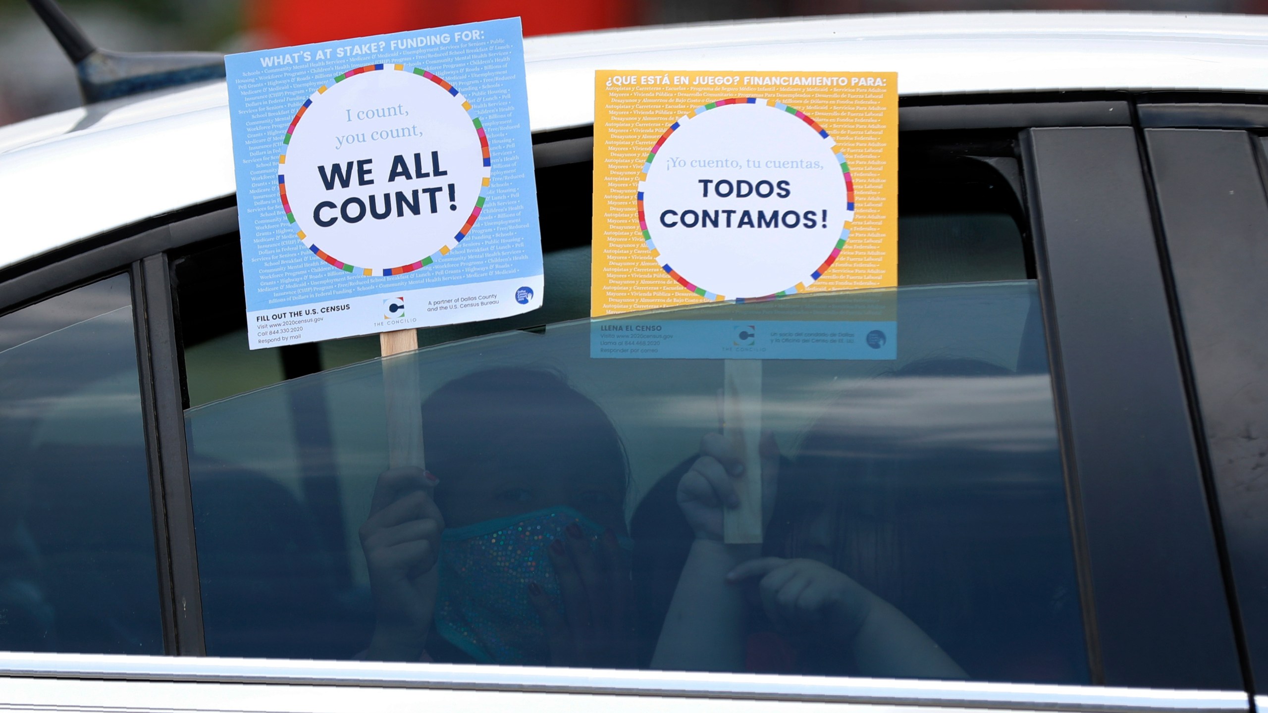 FILE - Two young children hold signs through the car window that make reference to the 2020 U.S. Census as they wait in the car with their family at an outreach event in Dallas, June 25, 2020. (AP Photo/Tony Gutierrez, File)