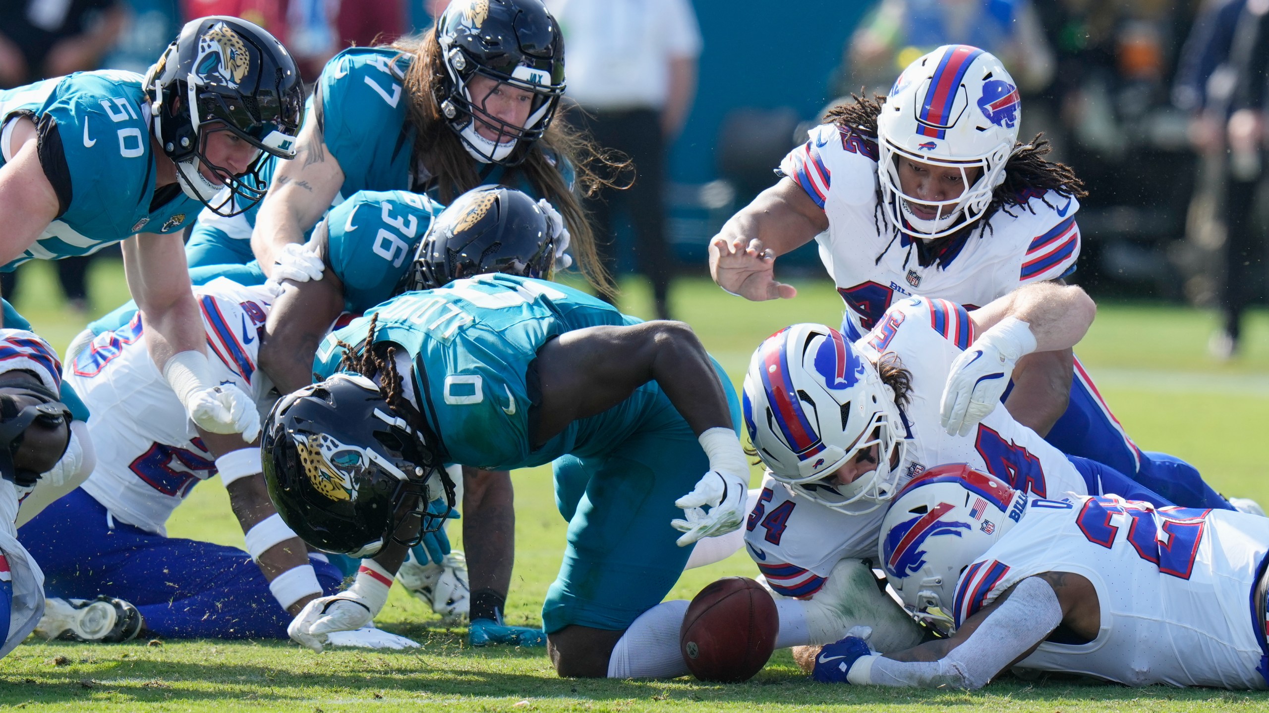 Buffalo Bills' Ray Davis, bottom right, fumbles a kickoff return from the Jacksonville Jaguars as teammate Baylon Spector (54) and Jacksonville Jaguars' Devin Lloyd (0) try to recover the ball during the first half of an NFL wild-card playoff football game Sunday, Jan. 11, 2026, in Jacksonville, Fla. (AP Photo/Chris O'Meara)