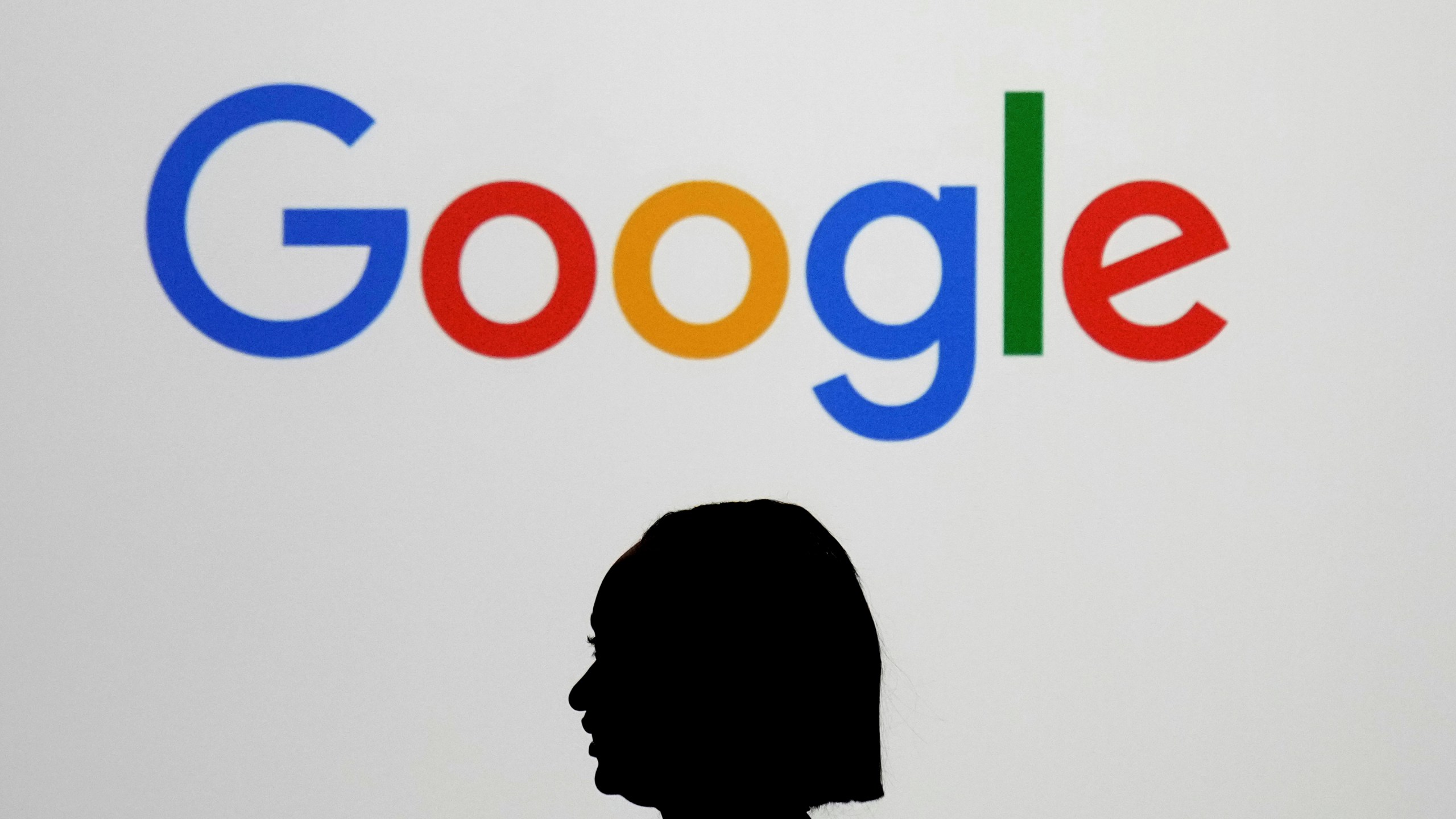 FILE - A woman walks by a giant screen with a logo at an event at the Paris Google Lab on the sidelines of the AI Action Summit in Paris, on Feb. 9, 2025. (AP Photo/Thibault Camus,File)