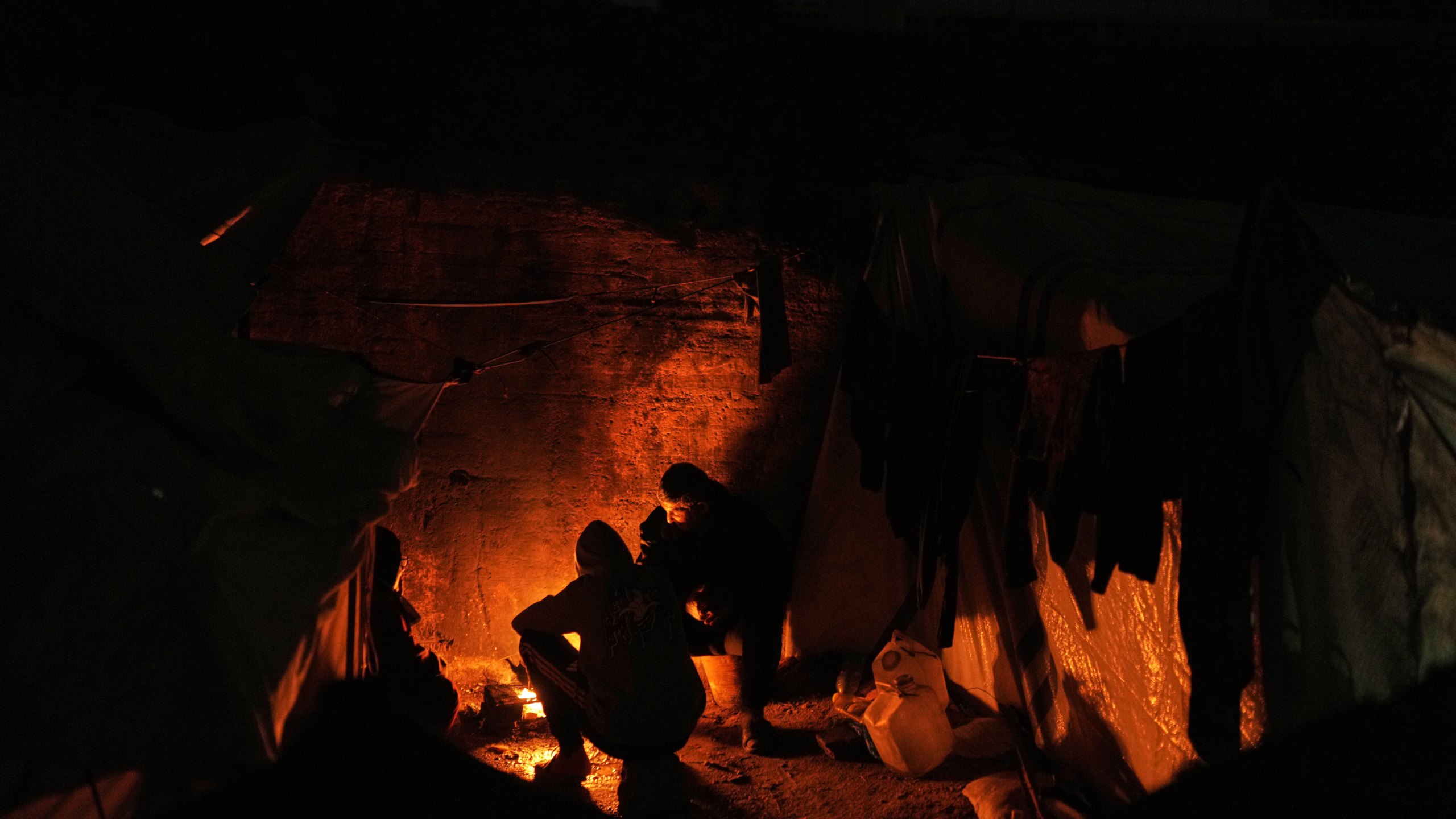 Displaced Palestinians cook and warm themselves around a fire at a tent camp in Gaza City, Sunday, Jan. 18, 2026. (AP Photo/Jehad Alshrafi)