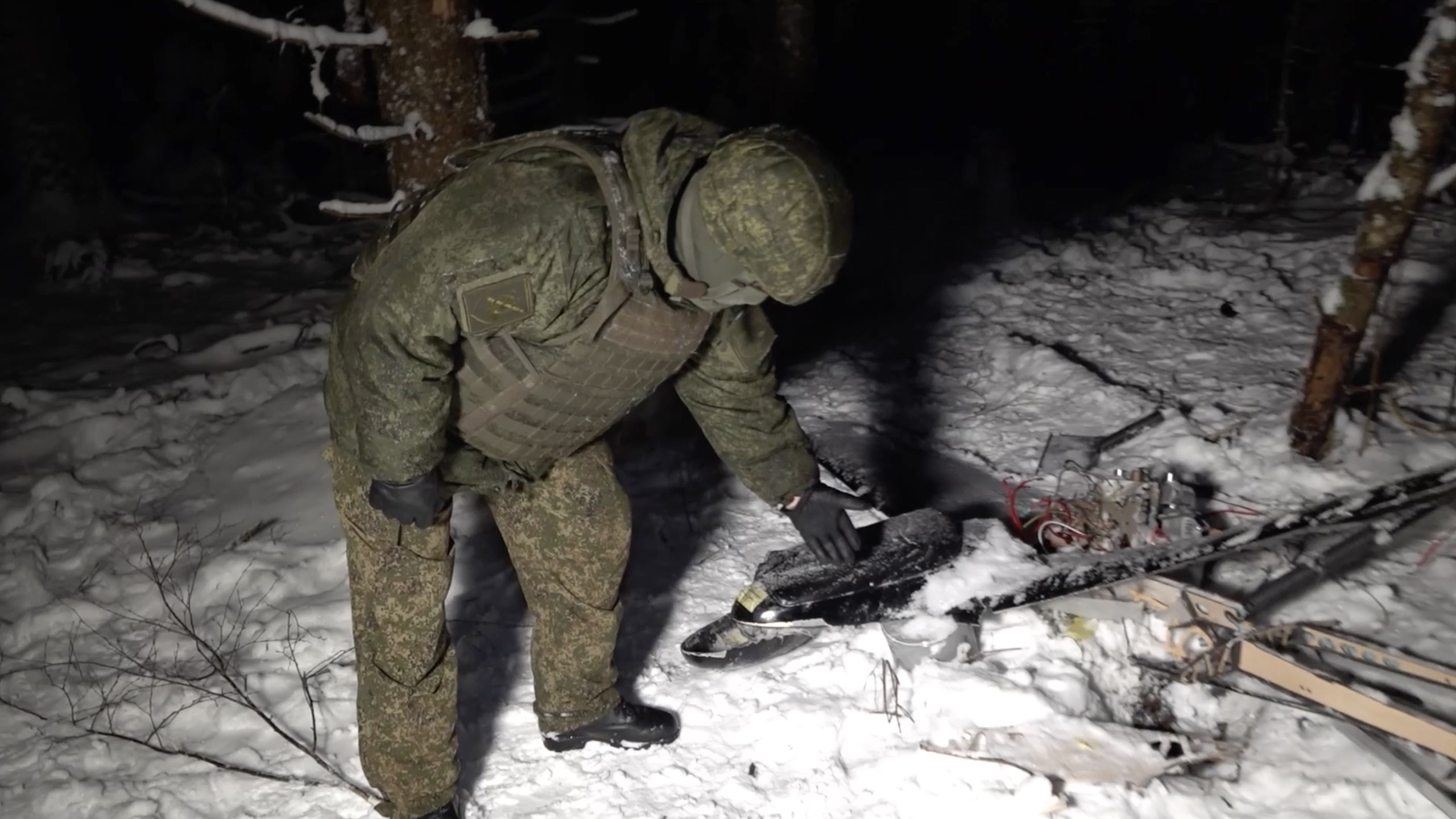 Russian soldier standing over drone wreckage in snow