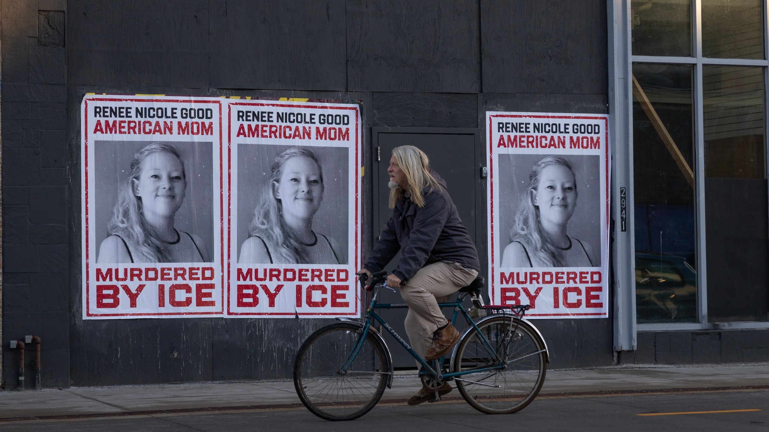 A cyclist rides past posters of Renee Good