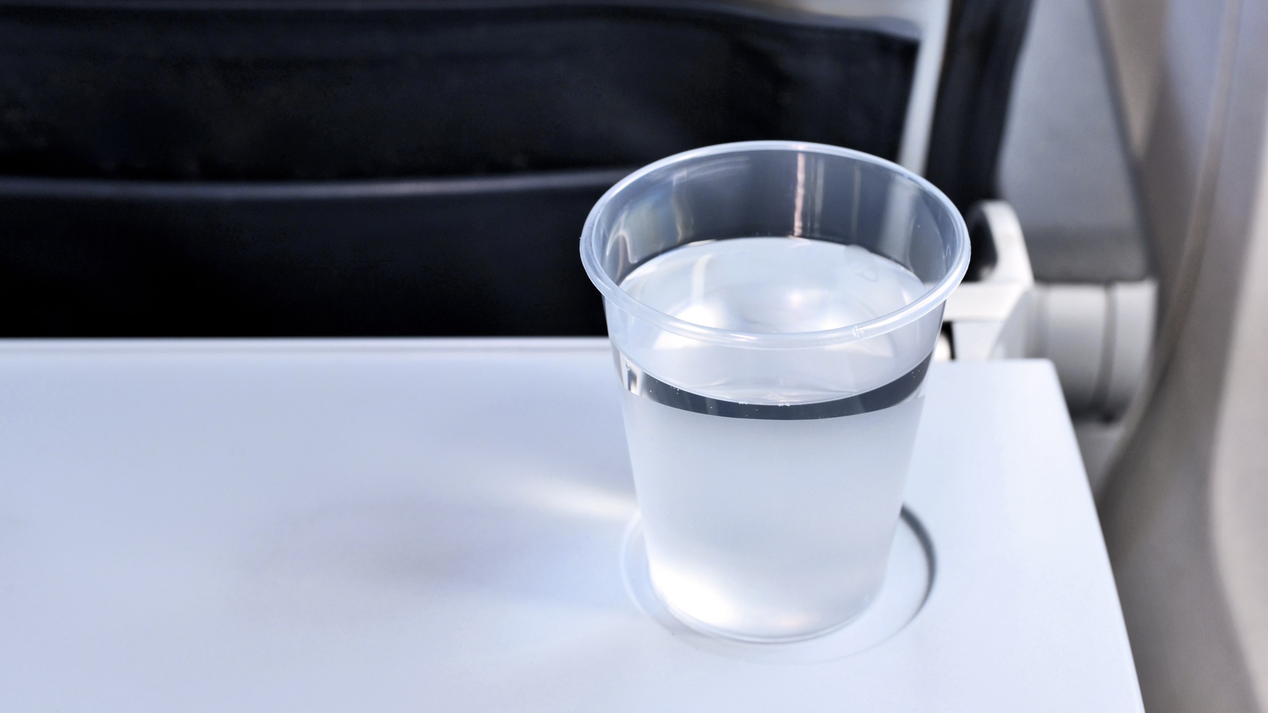 A plastic cup of water on an airplane folding tray